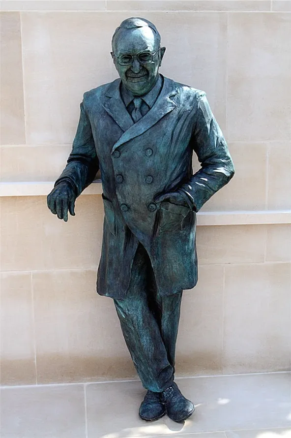 Life size bronze statue of Sir Ludwig Guttmann, leaning on a stone ledge and smiling